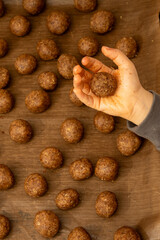 Top view of a child's hand holding a round ball of raw hazelnut cookie dough. Forming homemade Christmas treats