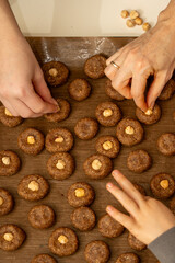 Top view of kid's hands carefully decorating raw cookies with hazelnuts. Fine motor skills and holiday fun