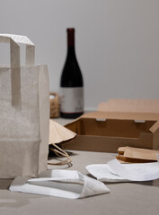 Horizontal shot of a white paper shopping bag mockup with delivery boxes and a blurred wine bottle,...