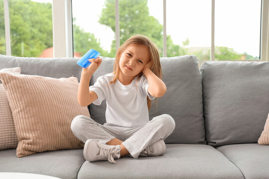Little girl with pediculosis and head lice comb sitting on sofa at home