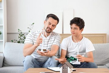 Fototapeta premium Teenage boy and his father talking about turbine models on sofa at home