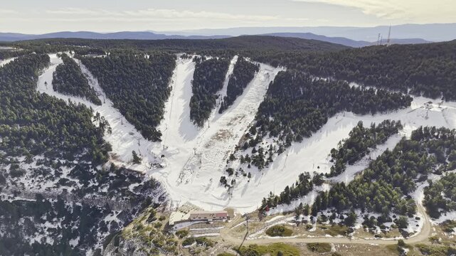Drone approaching a snowy ski slope in a dense pine forest, showing mountain terrain, winter sports area, chairlifts, ski trails and peaceful alpine scenery, ideal for winter travel, outdoor sports