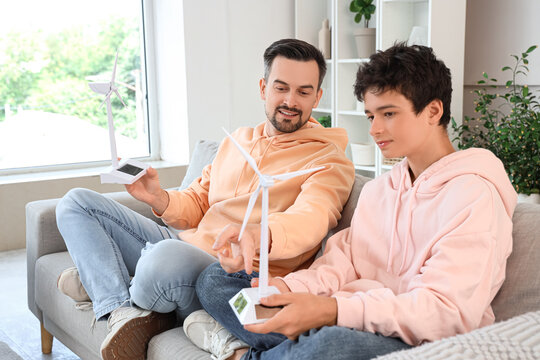 Teenage boy and his father talking about wind turbine models on sofa at home