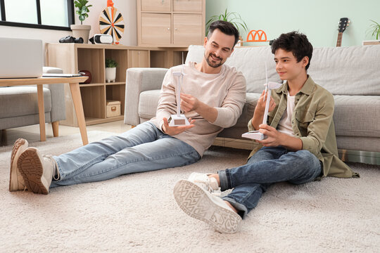 Teenage boy and his father with wind turbine models sitting on floor at home