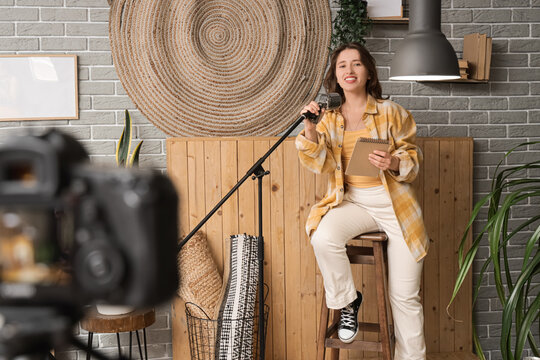 Female standup comedian with notebook and microphone recording video at home