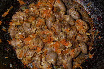 Close-up of fried chicken hearts cooked with onions and carrots. Chicken hearts being cooked in a pan with carrots and onions. Warm tones, natural food, cooking process.