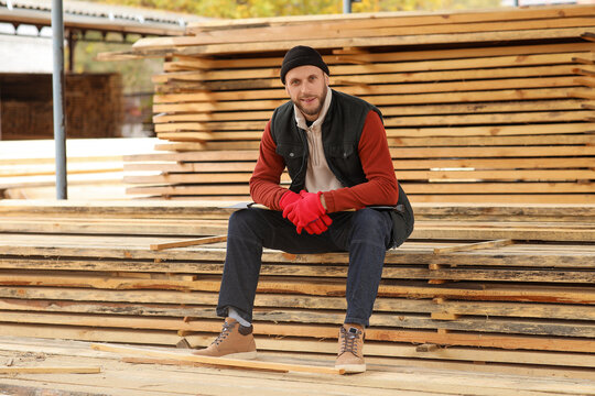 Male carpenter sitting on wooden planks at sawmill