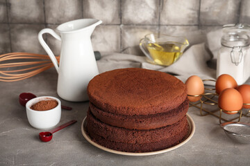 Delicious chocolate sponge cake cut into layers with ingredients and kitchen utensils on grey grunge background