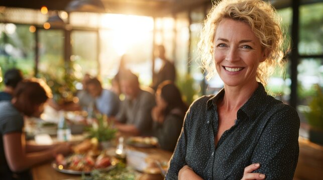 Happy entrepreneur woman smiling, arms crossed, overseeing busy restaurant with warm evening light. - Powered by Adobe
