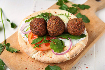 Cutting board of delicious pita with falafel and fresh vegetables on white wooden background, closeup