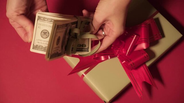 Gift box and stack of dollars on red background, representing cash gifts for Christmas, New Year, Valentines Day, celebrations, personal finance, gifting, savings and special holiday events