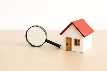 Housing market analysis with magnifying glass near miniature home representing research rent buying selling and real estate choices