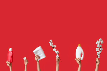 Female hands with cotton flowers, towel and laundry detergents on red background