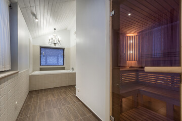 A spacious bathroom features a luxurious sauna and a large tub. Elegant lighting, wooden accents, and contemporary design create a relaxing atmosphere in this private retreat.