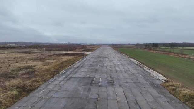 A deserted concrete runway of a former Soviet military airbase in Kedainiai, Lithuania. Overcast sky, rural fields, and decaying aviation infrastructure