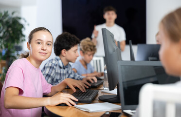 Fototapeta premium Smiling preteen girl sitting at computer table together with other attendees of IT courses