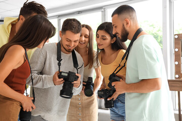 Group of young photographers with cameras looking at pictures during courses in studio