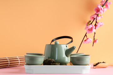 Tray with teapot, cups of tea, dry pressed puer leaves, bamboo mat and plum blossom branch on color background