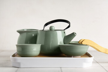 Tray with teapot, cups of tea, jug and bamboo tongs on white tile table