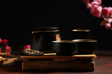Tray with teapot, cups of tea, dry pressed puer leaves and plum blossom branches on red grunge...