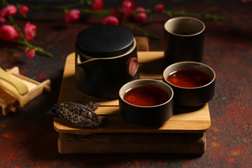 Tray with teapot, cups of tea, dry pressed puer leaves and plum blossom branches on red grunge background