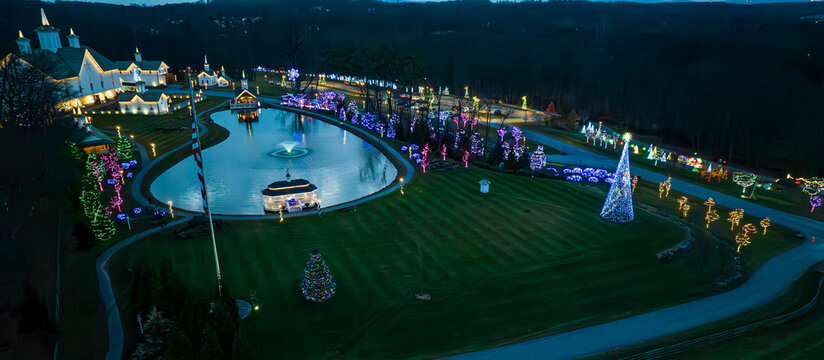 Colorful holiday lights decorate trees and buildings around a peaceful pond. Visitors enjoy the festive atmosphere as they stroll in this beautifully lit park.