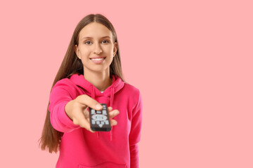 Young woman with remote controller watching TV on pink background