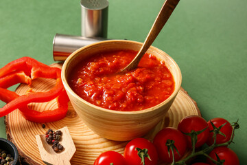 Wooden tray with bowl of tasty tomato sauce and ingredients on green background, closeup