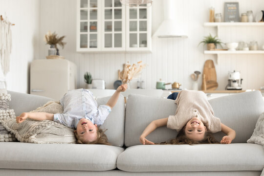 Cute diverse little siblings hanging over back of large sofa - Powered by Adobe