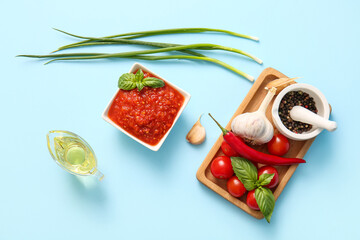 Bowl of tasty tomato sauce and ingredients on blue background