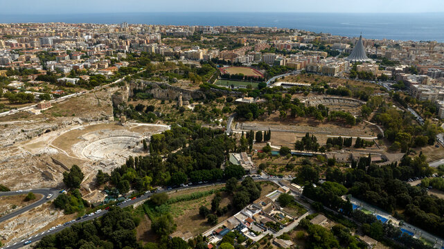 Aerial view of the Neapolis Archaeological Park, located in Syracuse, Sicily, Italy. In the background, at horizon, there's the modern city overlooking the Mediterranean Sea. Sunny summer morning.