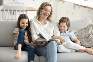Smiling mom reading book to little daughter son on couch