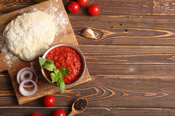Board with bowl of tasty tomato sauce and raw dough on white wooden background