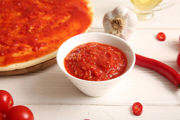 Bowl of tasty tomato sauce and ingredients on white wooden background, closeup