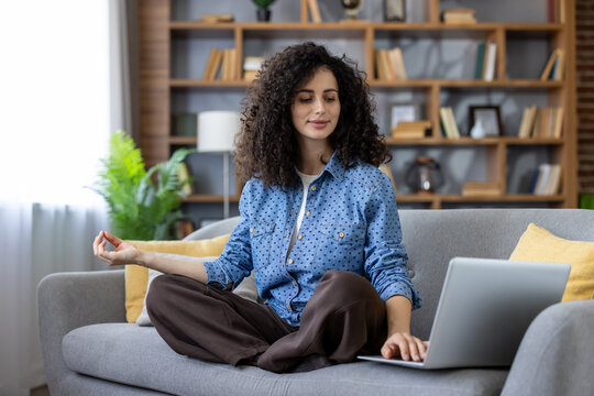 Young woman practicing mindfulness and finding balance while working remotely on a laptop from a cozy home office couch, calm and focused during a wellness break - Powered by Adobe