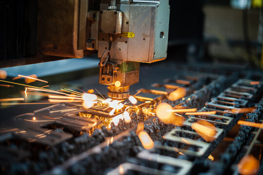 Laser cutting process with digital software control. The laser cutter head cuts through a sheet of metal, sending sparks. High quality photo