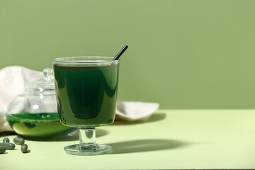 Glass of spirulina drink with pills, jar and powder on green background