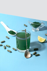 Glass of spirulina drink with pills, gravy boat, spoon, lime slice and powder on color background