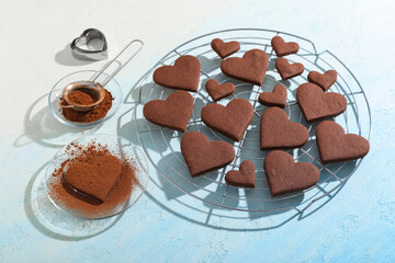 Glass plate and stand with sweet chocolate heart-shaped cookies on light blue background. Valentine's Day celebration