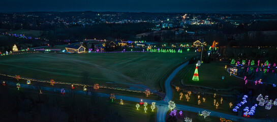 A vibrant display of holiday lights illuminates a spacious park during the evening. Multicolored decorations create a festive atmosphere, attracting visitors to enjoy the seasonal cheer.