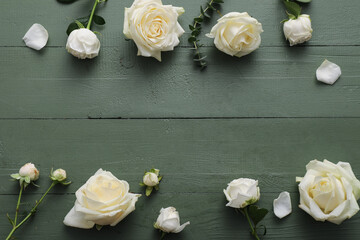 Naklejka premium Frame made of beautiful white roses and eucalyptus branch on green wooden background