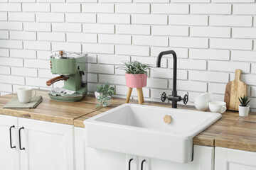 Sink with coffee machine and artificial plants on counter near white brick wall in kitchen