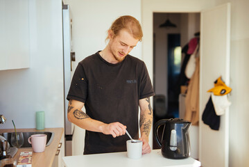 Peaceful evening in kitchen as young man stirs his hot beverage