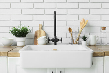 Sink with utensils and artificial plants on counter near white brick wall in kitchen