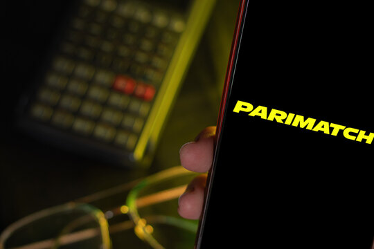 Phone with the Parimatch logo held in front of a calculator and glasses, composition associated with betting and e-sports brands