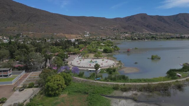 Aerial forward movement over the malecon in Jocotepec, showing pathways, trees and calm lake scenery