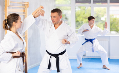 Man and woman train to perform basic defensive installations and attacking actions during combat techniques classes. Young male coach comments and corrects mistakes of students