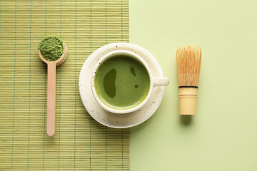 Cup of fresh matcha tea with scoop, powder and chasen on green background