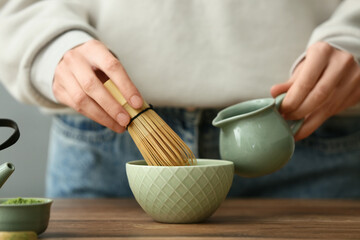 Woman preparing matcha tea at wooden table in kitchen