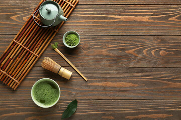 Bowl of fresh matcha tea with powder, chasen, chashaku and teapot on wooden background